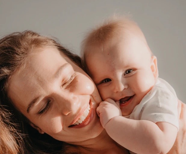 A smiling mother cuddling her happy baby cheek to cheek